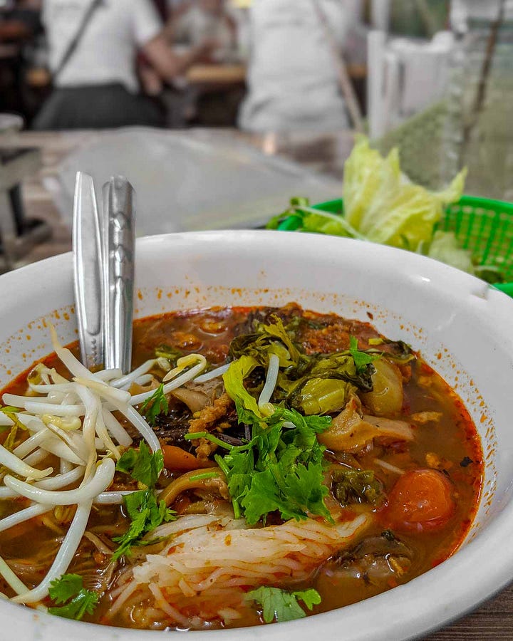 bowl of soupy red curry with chunks of small tomatoes, fresh coriander, and bean sprouts