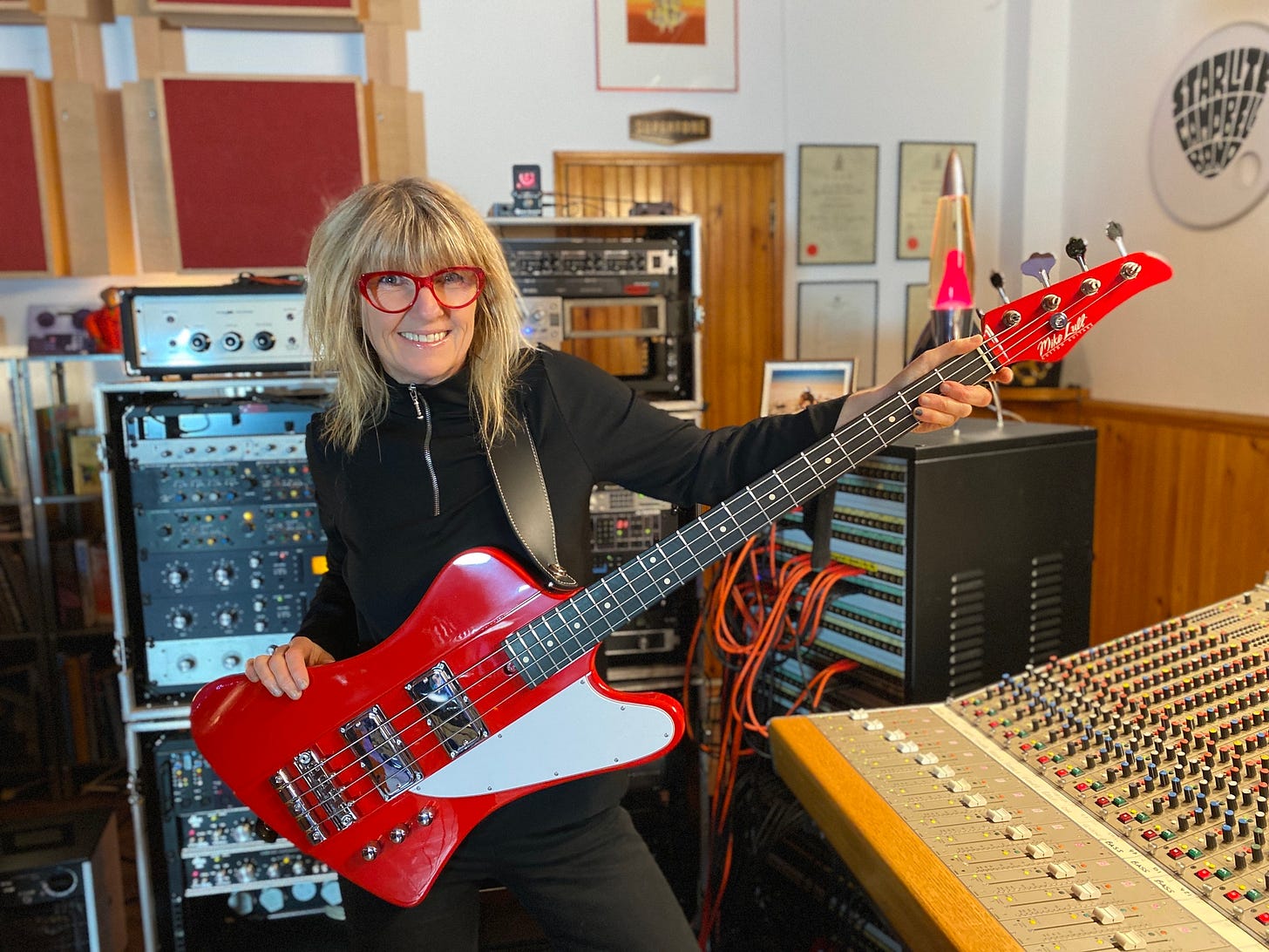 Suzy Starlite pictured with her Mike Lull T4 Starlite bass in signal red against the backdrop of the Supertone recording studio