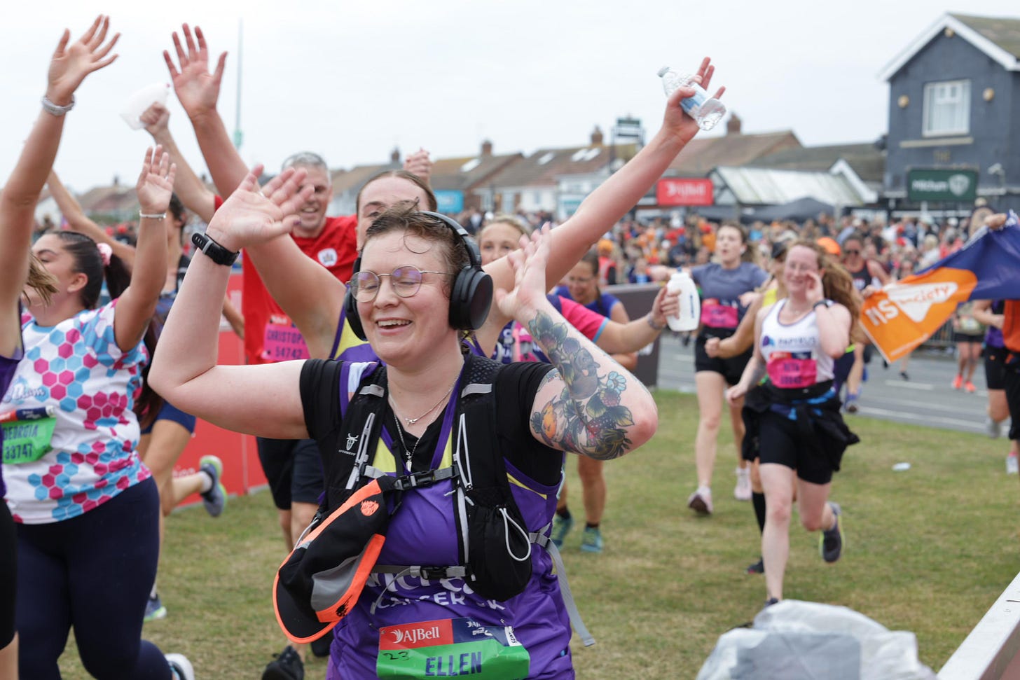 Event photo of Ellen, hands in the air, wet hair, eyes closed and smiling with intense relief, surrounded by other runners, she is looking exhausted but very, very happy.
