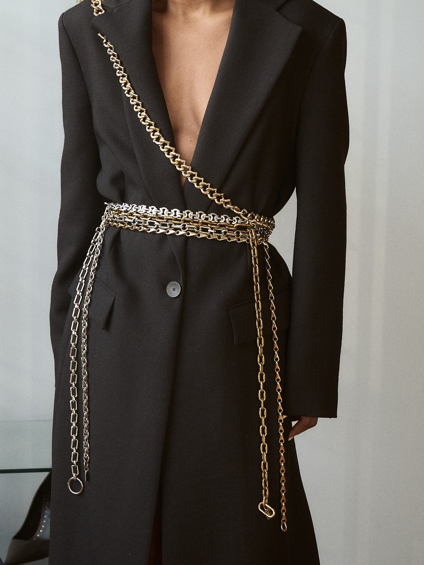 Model wearing a long black wool coat styled with the Lapo Lounge Eris, Hyperion, Himalia, and Zira chain belts layered at the waist.