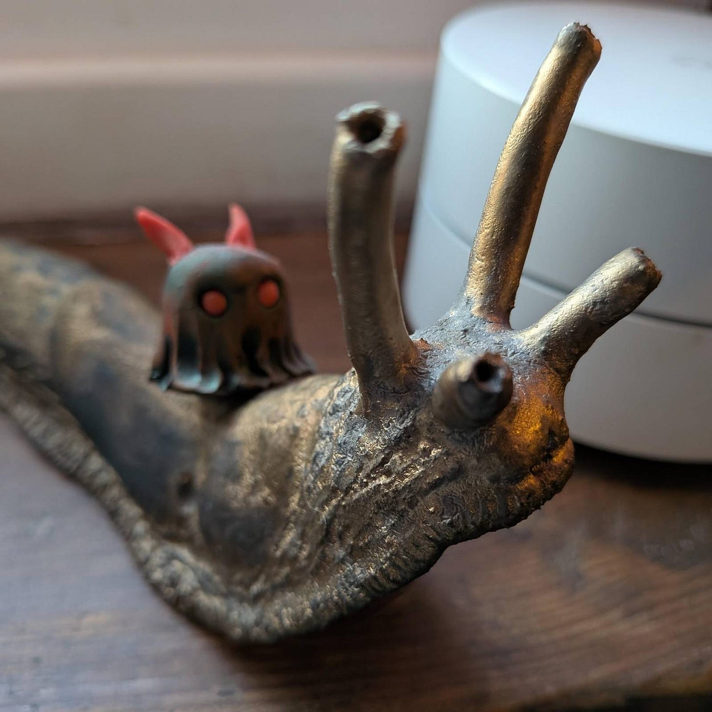 A Fimo black demon ghostie is riding a golden slug statue on a window ledge A Fimo black demon ghostie is riding a golden slug statue on a window ledge