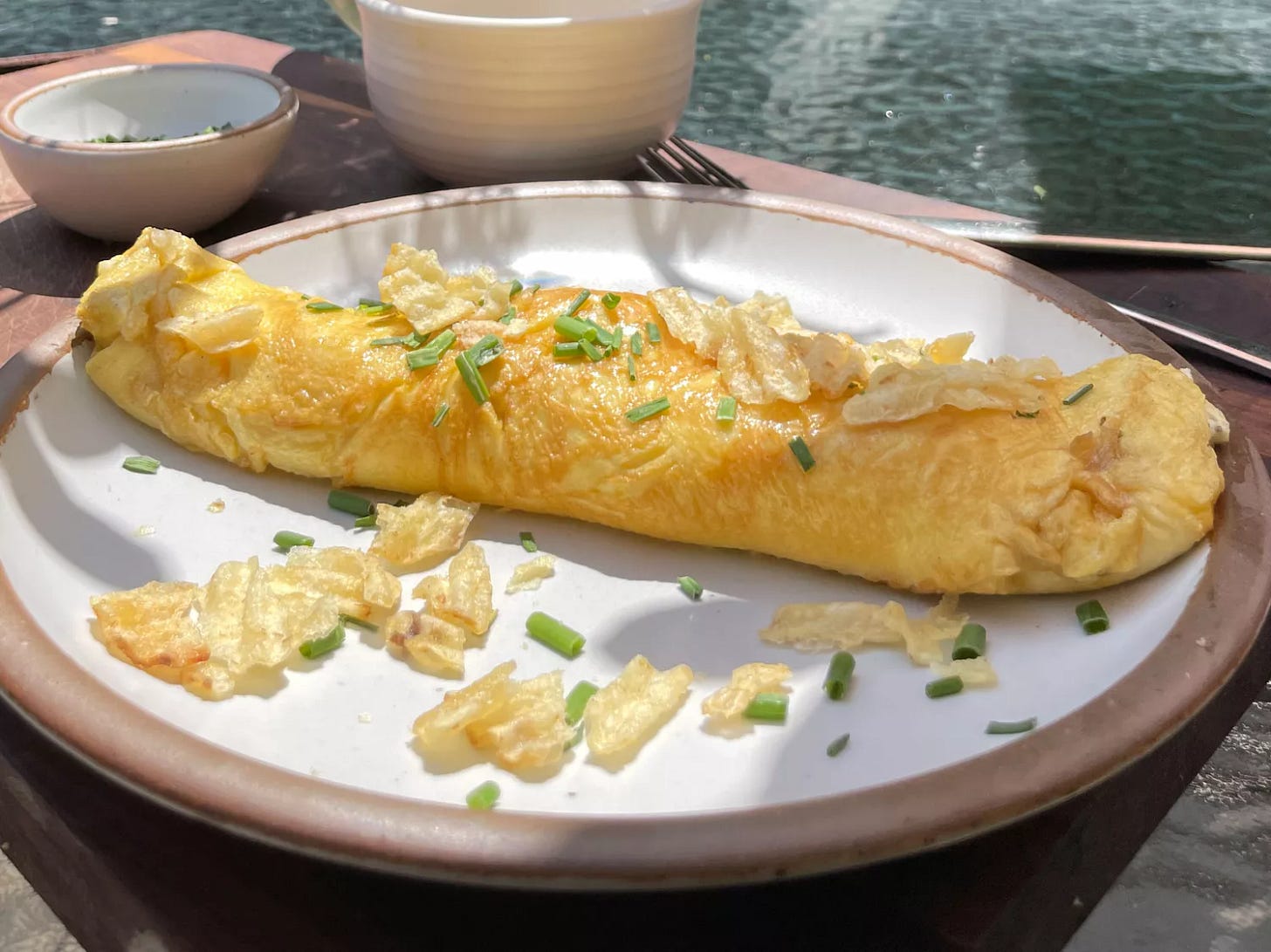 A French omelet topped with crushed potato chips and fresh chives on a white plate on a patio table A French omelet topped with crushed potato chips and fresh chives on a white plate on a patio table