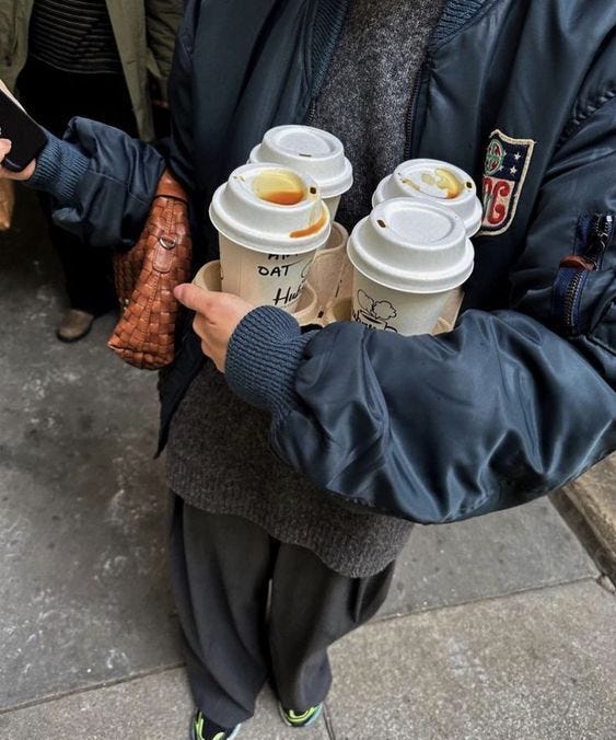This may contain: a man holding two cups of coffee in his hands while standing on the sidewalk with other people