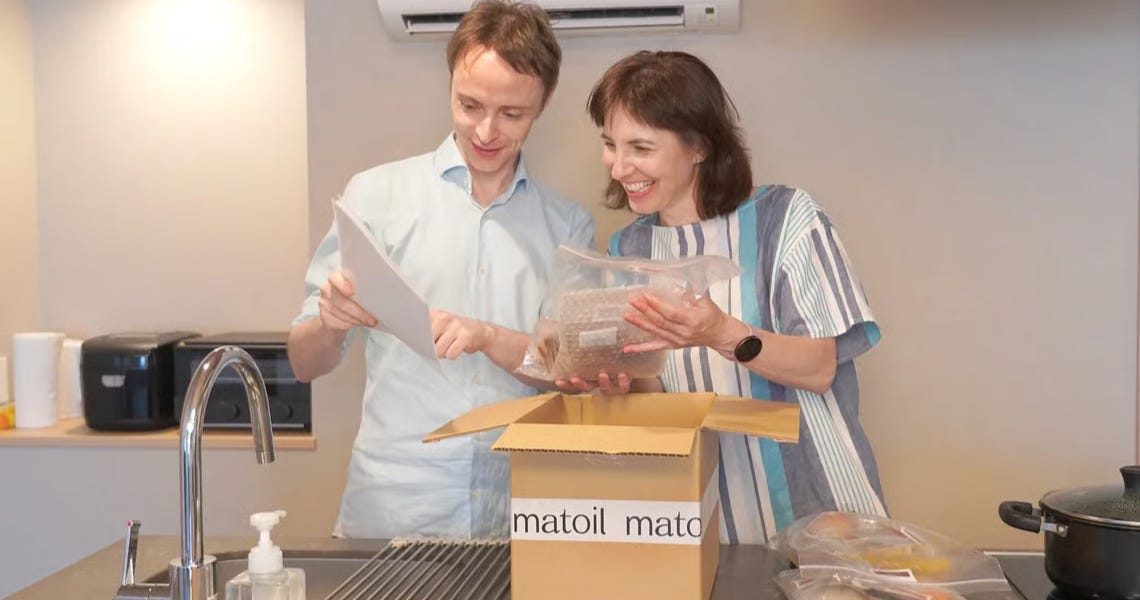 A man and a woman reading from instructions and taking items from a brown box with matoil written on it. 