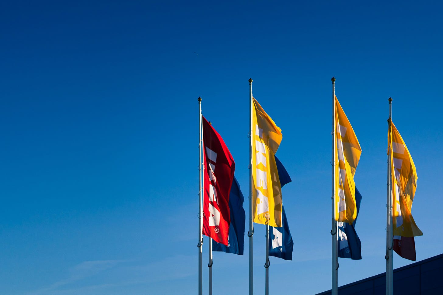IKEA flags waving against clear blue sky with one red flag and three yellow flags displaying the company logo outside store entrance - business management and entrepreneurship example