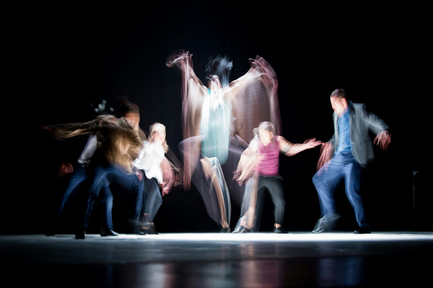 A group of people moving together in a dark space, their overlapping, motion-blurred bodies making the boundaries between them difficult to distinguish.