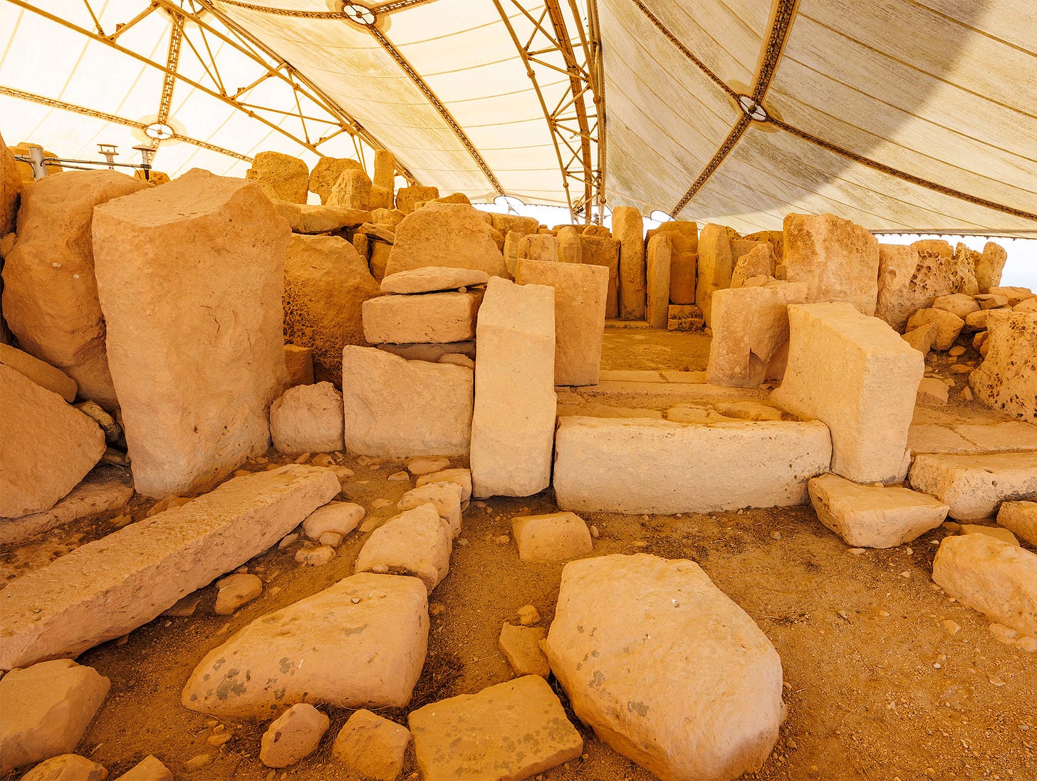 Interior view of Hagar Qim megalithic temple in Malta, showing massive limestone blocks under a protective canopy.