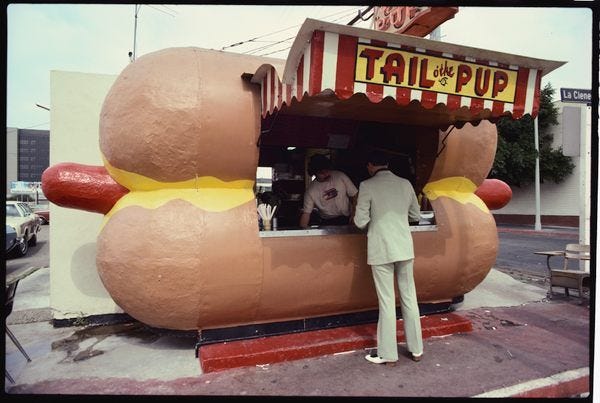 This may contain: a man standing in front of a giant hot dog stand with buns and ketchup on it