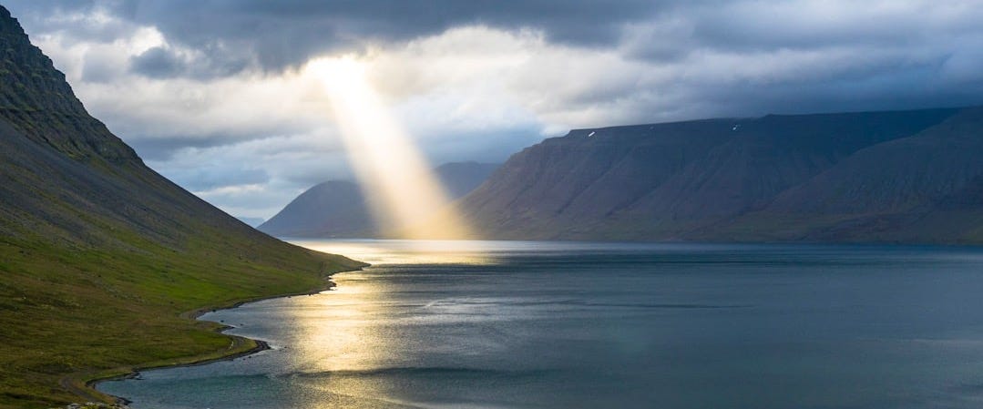 sun reflection on calm water near green mountains
