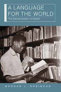 A book cover with a black and white photo of a man in a library, holding some books in one hand and reading from a book in the other.