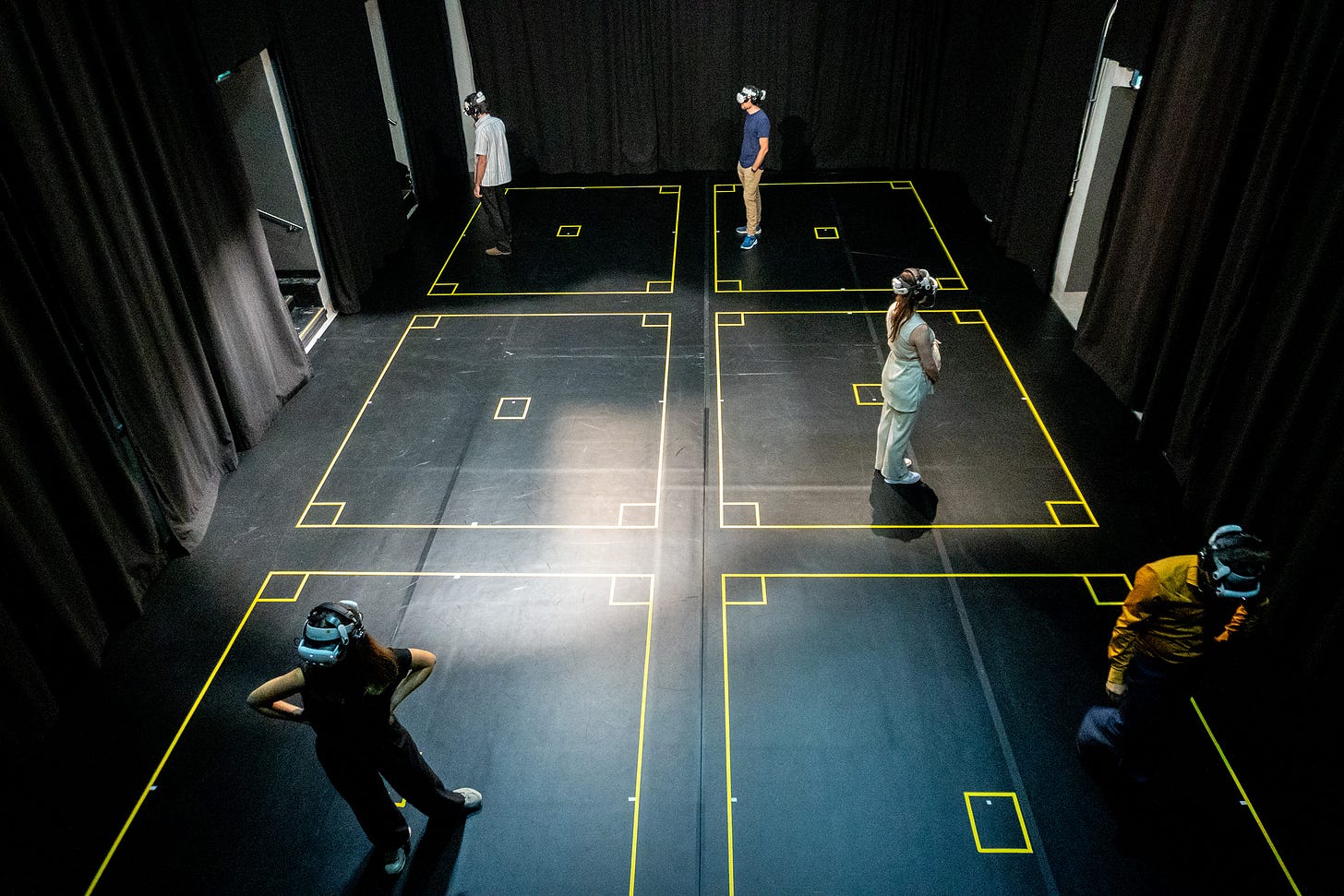 Audience members wearing VR headsets experience [EOL] End of Life, each standing within a small square which has been marked out on the floor.