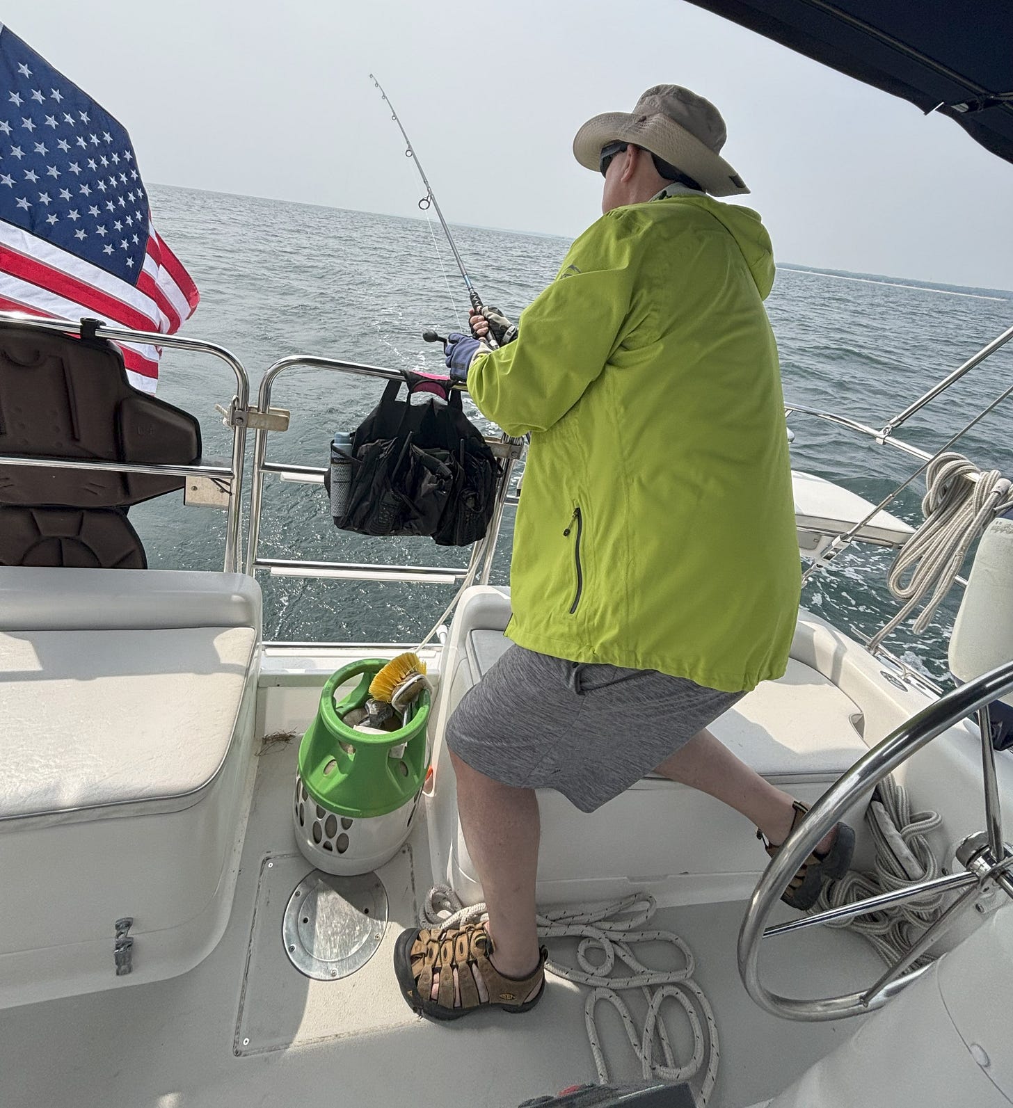 Man in yellow slicker fishing from a sailboat, rod in hand