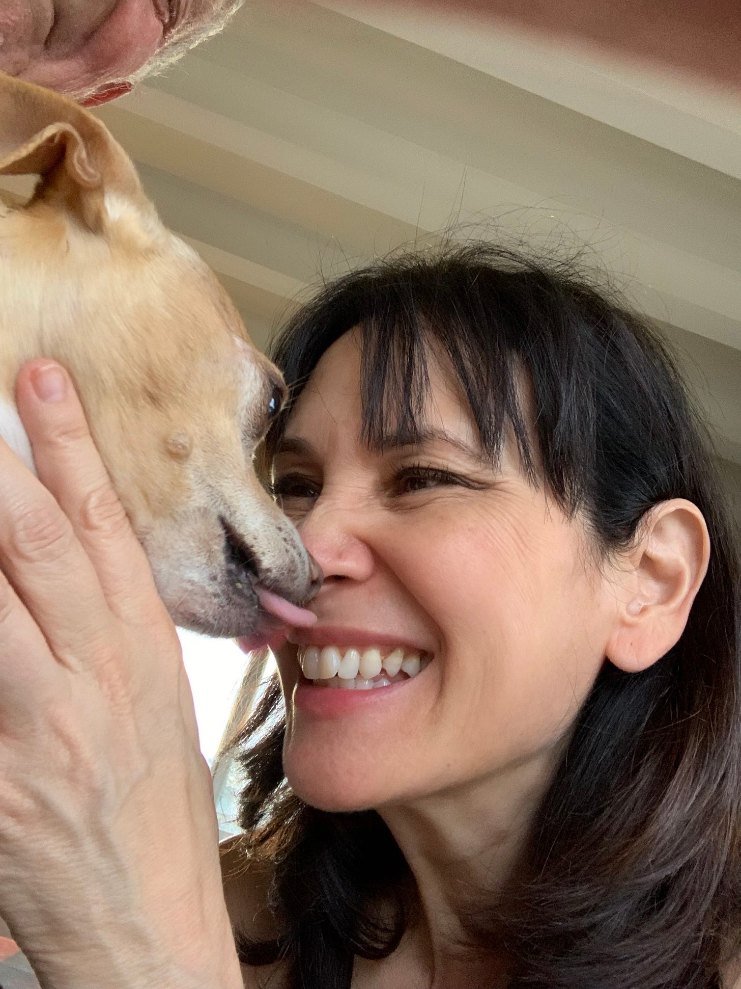 Laverne smiles joyfully as her small cream colored dog, Roo, playfully licks her nose.