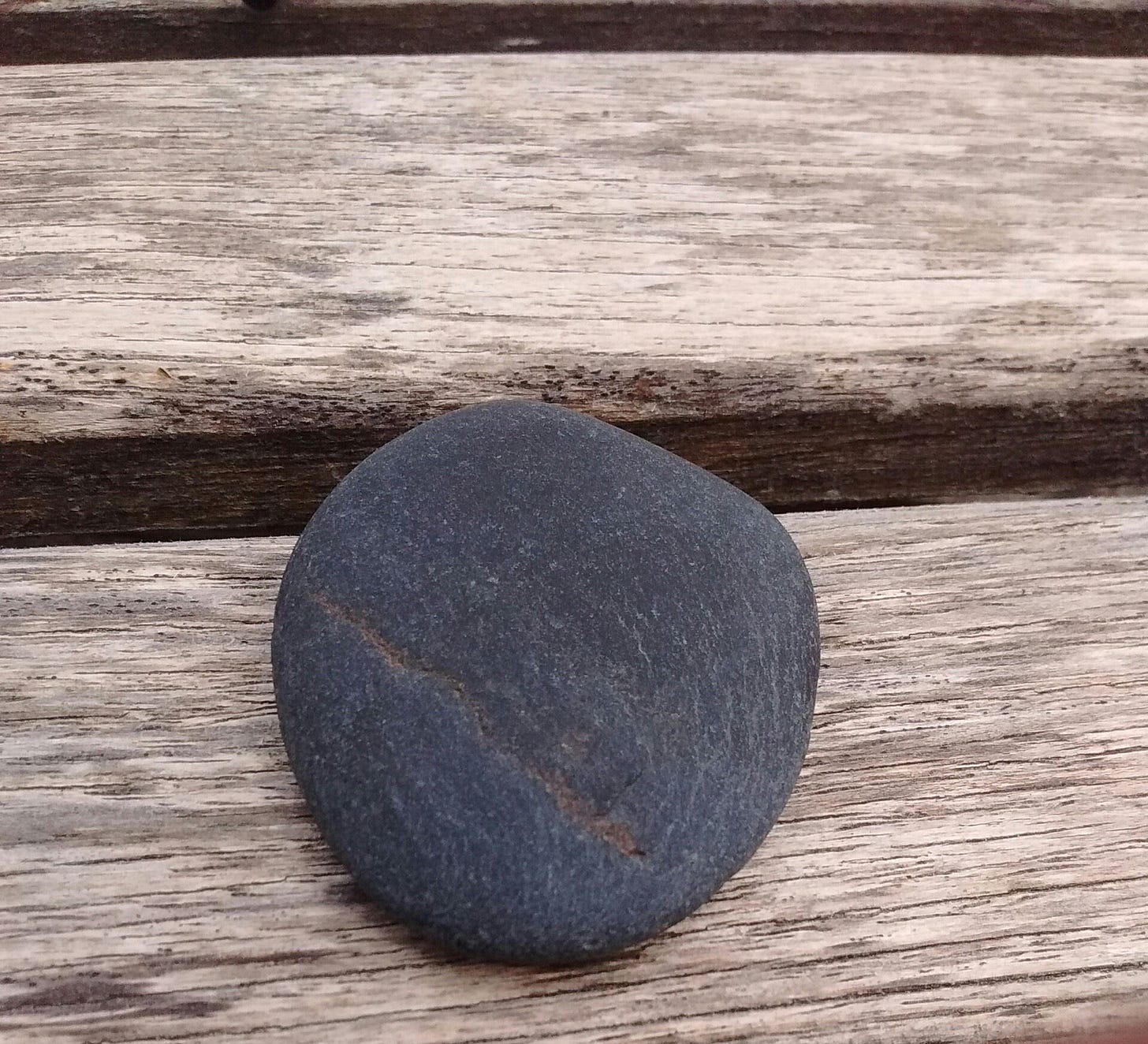 A slate grey pebble on a wooden picnic table. 