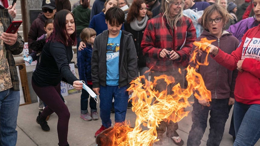 A protester tosses a surgical mask into a fire as others look on, some filming on mobile phones.