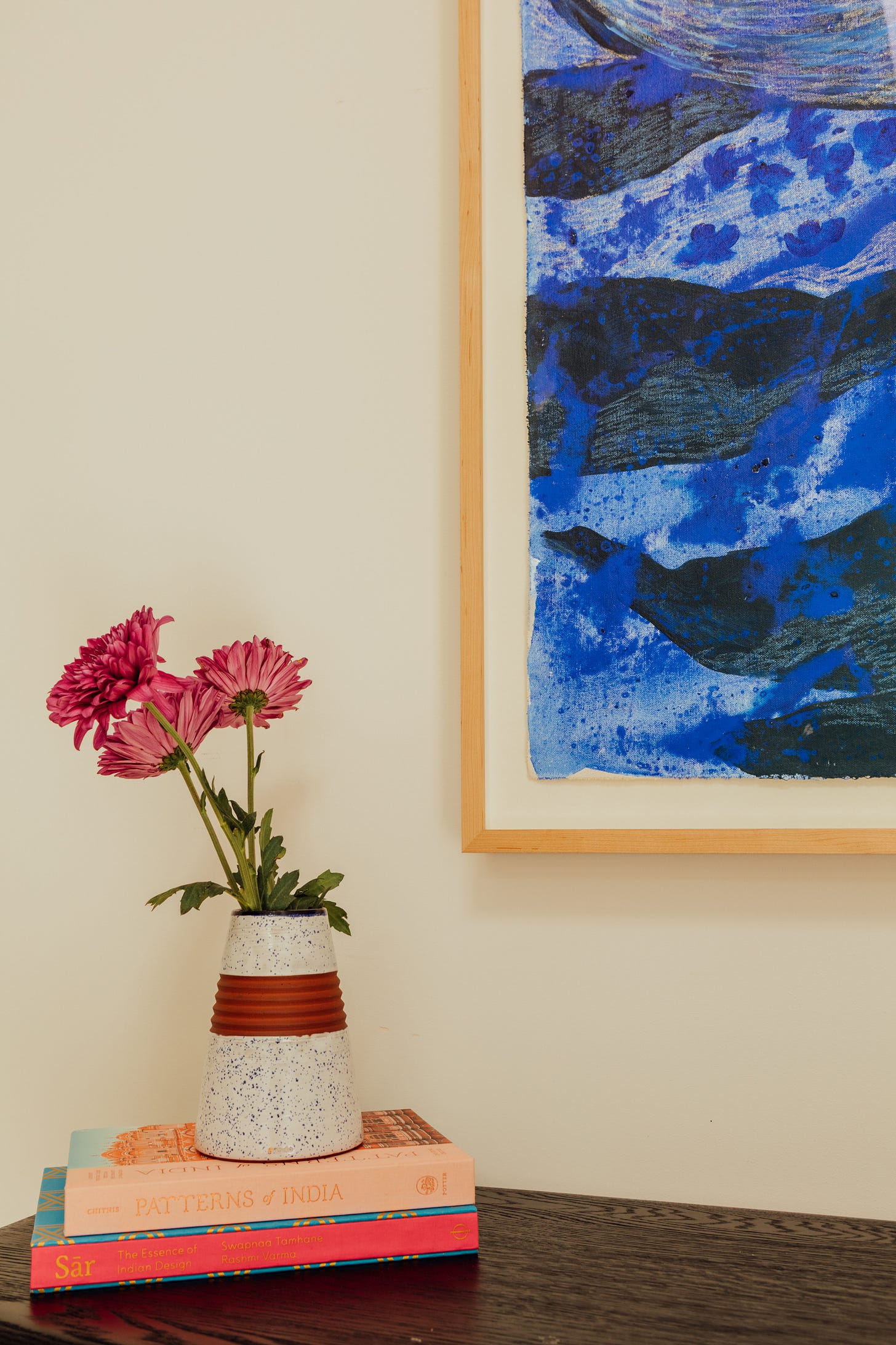 Close view of the lower left corner of Summer Nights, showing the raw canvas edge floating inside the light oak frame, beside pink dahlias in a speckled vase.