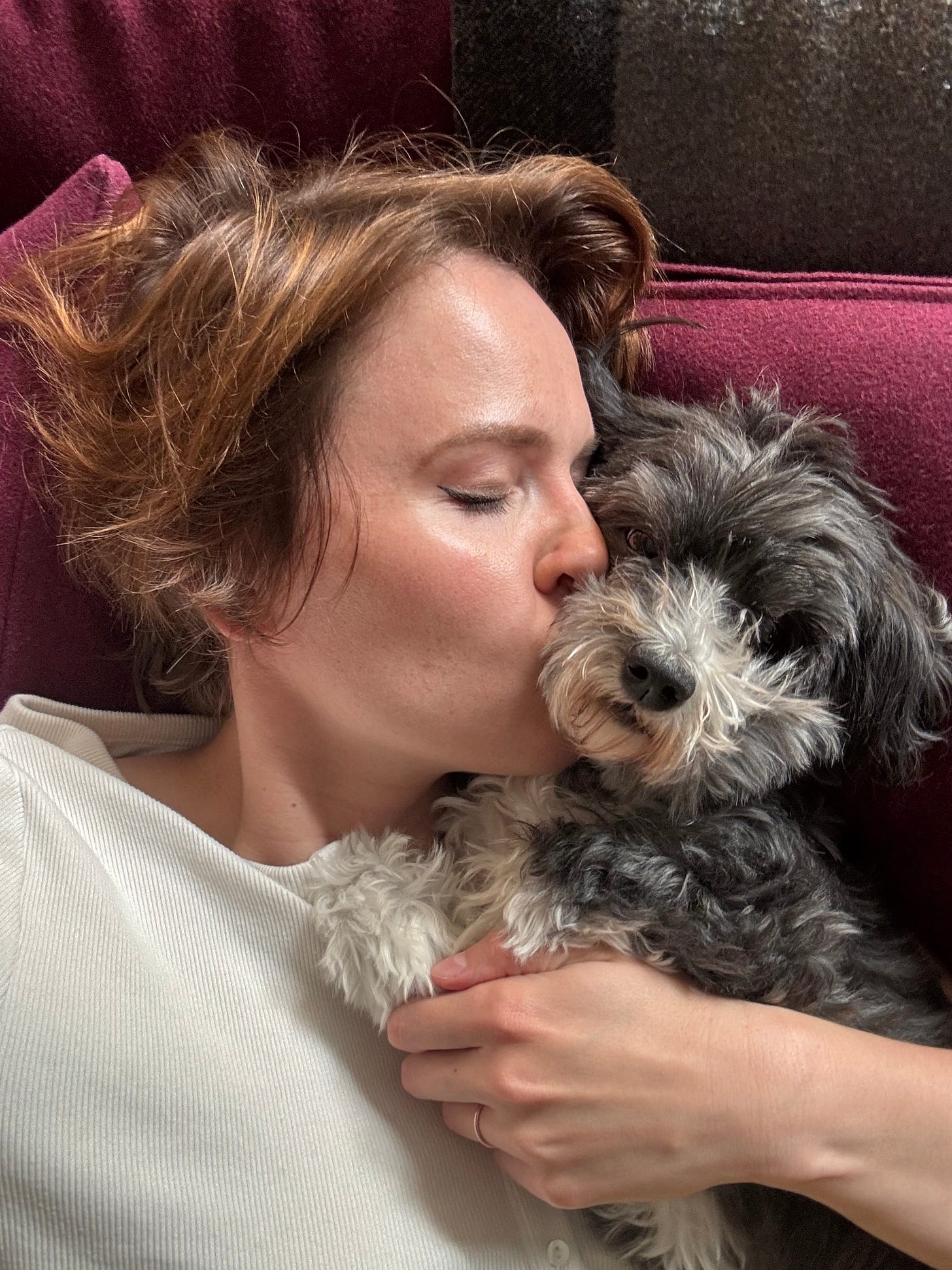 a close up of a woman (me) kissing a fluffy gray dog on the snout as they recline on a couch