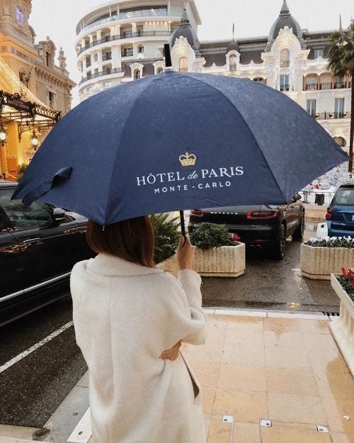 This may contain: a woman holding an umbrella in front of a hotel and paris monte - cendo