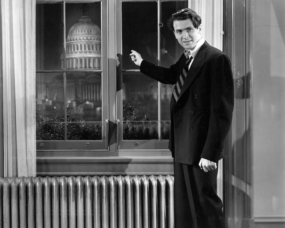 Jimmy Stewart as Jefferson Smith in Mr. Smith Goes to Washington (1939), standing by a window pointing toward the U.S. Capitol Building, symbolizing civic idealism and belief in American democracy.