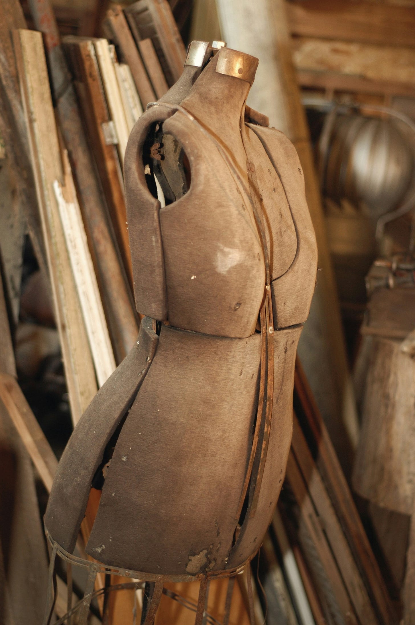 An old manequim stands in a wood workshop. The manequim seems to have the midsection cracked.