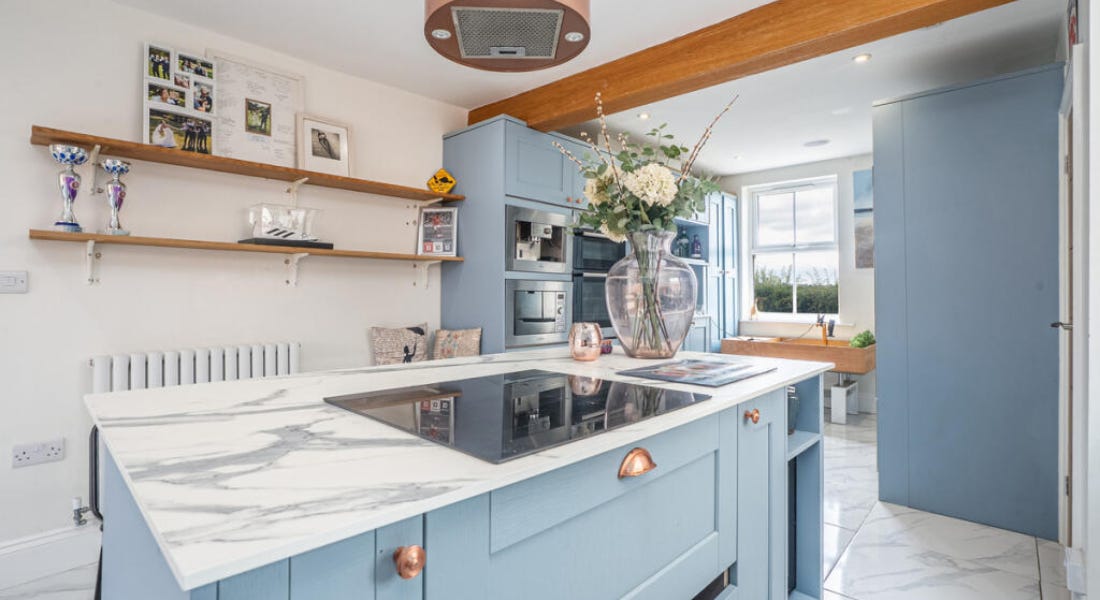 A kitchen with blue cabinets, copper handles, and marble flooring