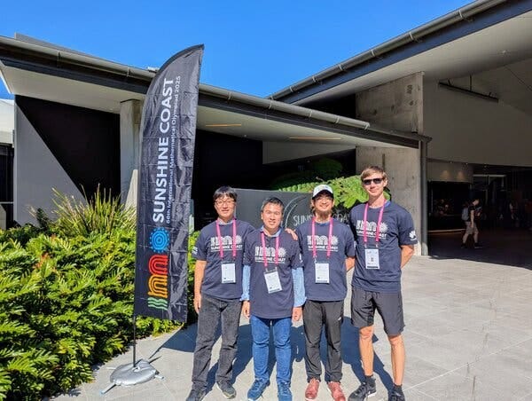 Four young men in blue shirts pose for a photo outside a building.