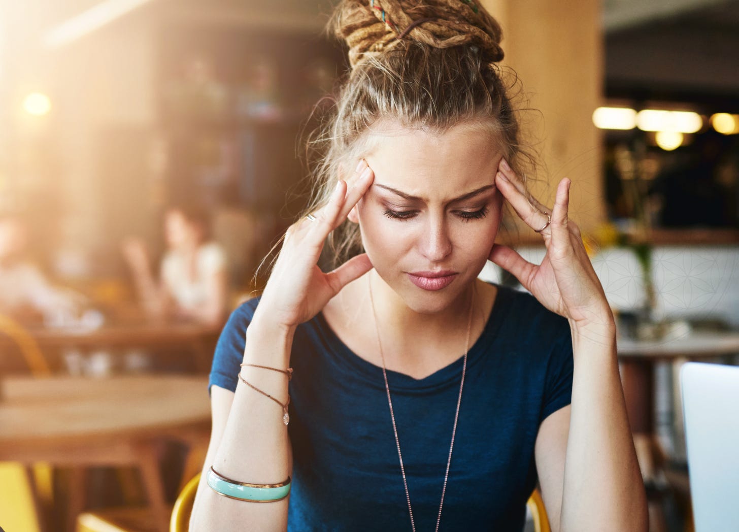 woman sitting alone in a cafe with her hands to her temples, overthinking