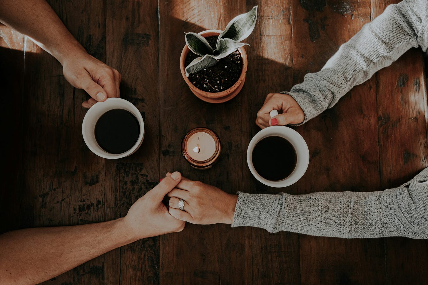 man woman holding hands and coffee mugs