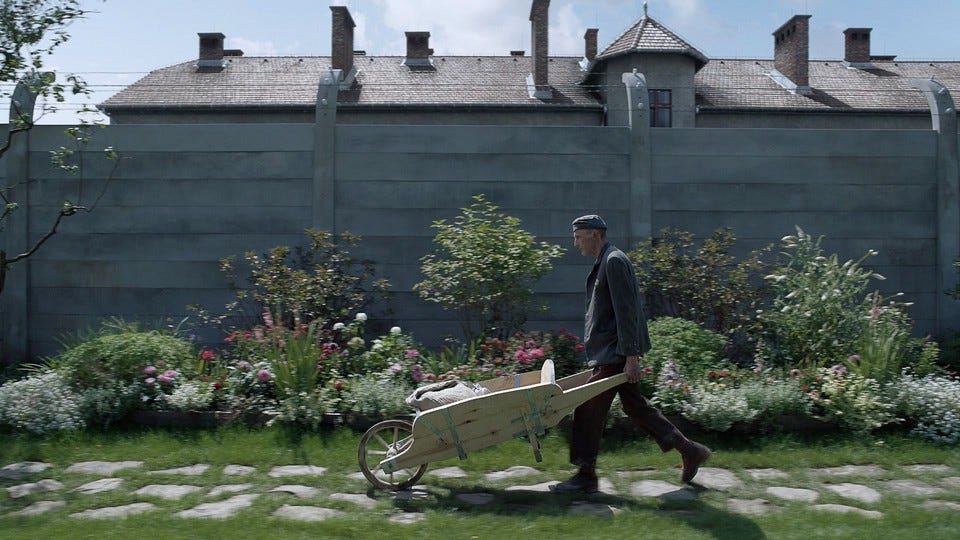 Christian Friedel as Rudolf pushing a wheelbarrow next to a wall with barbed wire Christian Friedel as Rudolf pushing a wheelbarrow next to a wall with barbed wire