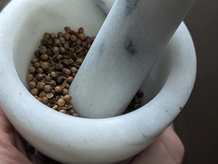 Whole coriander seeds and cumin seeds being dry-roasted and lightly crushed.