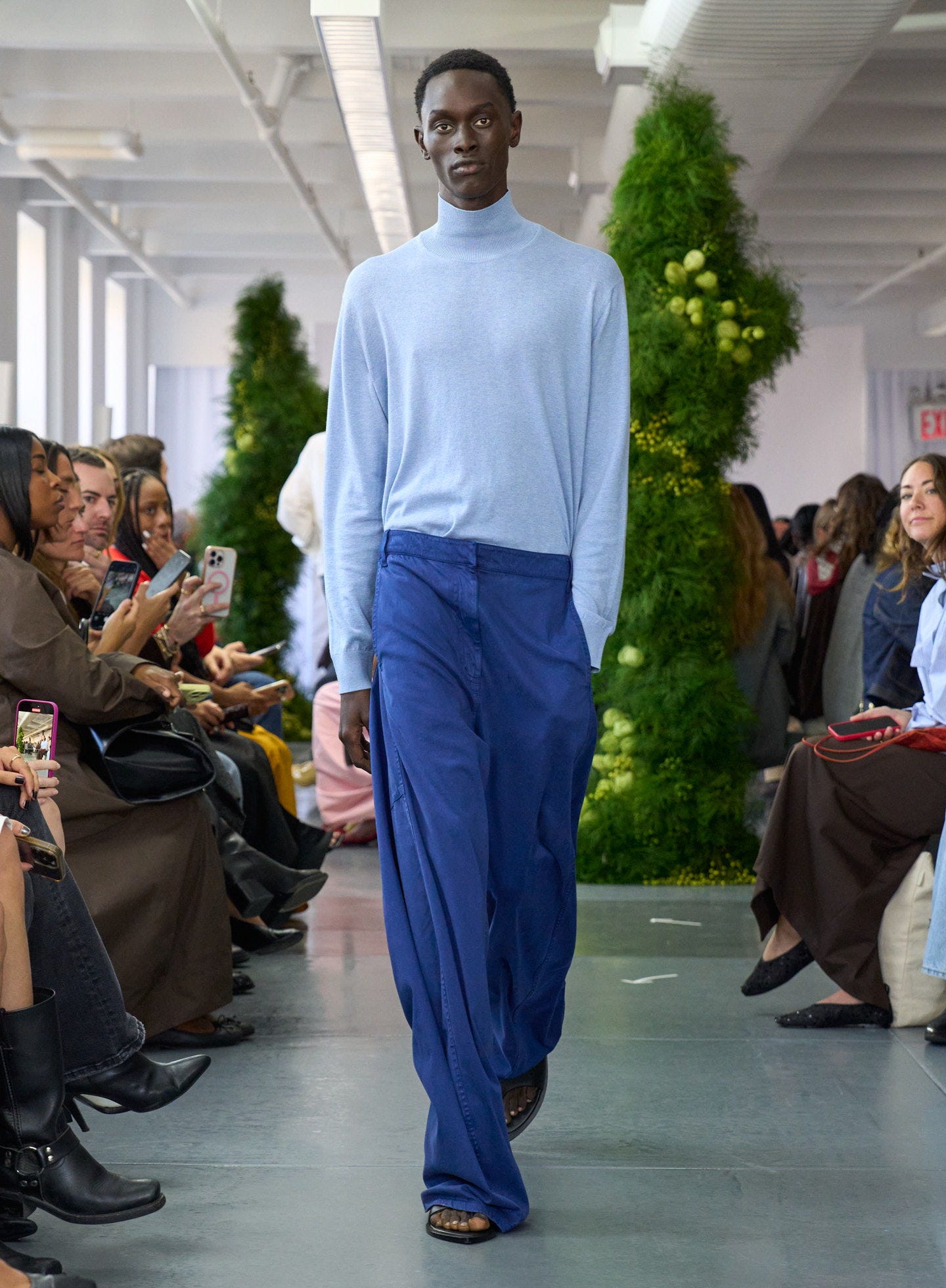Model walking down runway in light blue sweater and blue pants. Model walking down runway in light blue sweater and blue pants.
