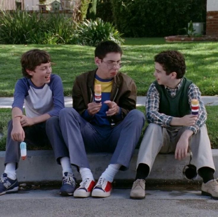 This may contain: three young men sitting on a curb eating ice cream