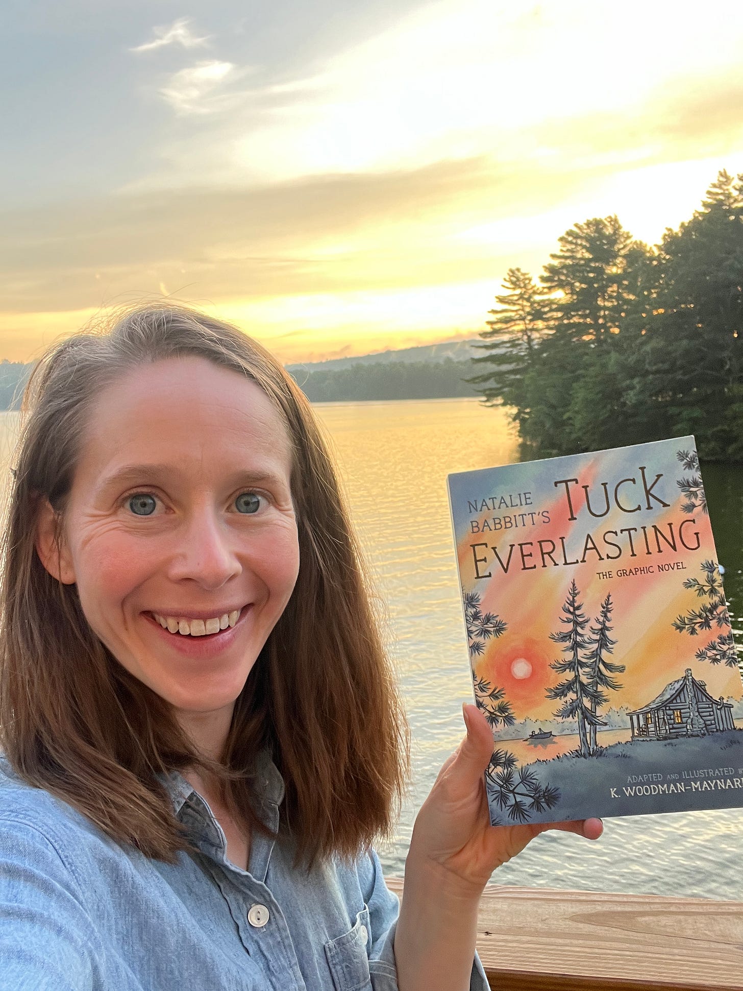 Graphic novelist K. Woodman-Maynard smiles as she holds her print copy of her graphic novel adaptation of Tuck Everlasting. 