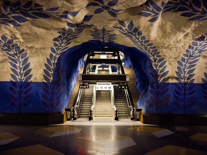 A four-image collage showing ornate and immersive metro stations around the world, including blue painted escalator walls, patterned vaulted ceilings, tiled station interiors, and a train platform with decorative lighting.