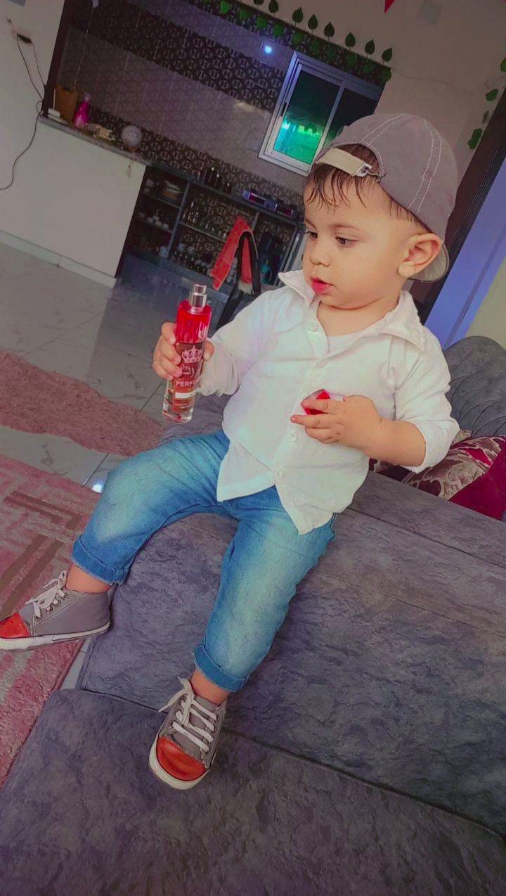a young boy in a shirt and jeans sits of the arm of a couch