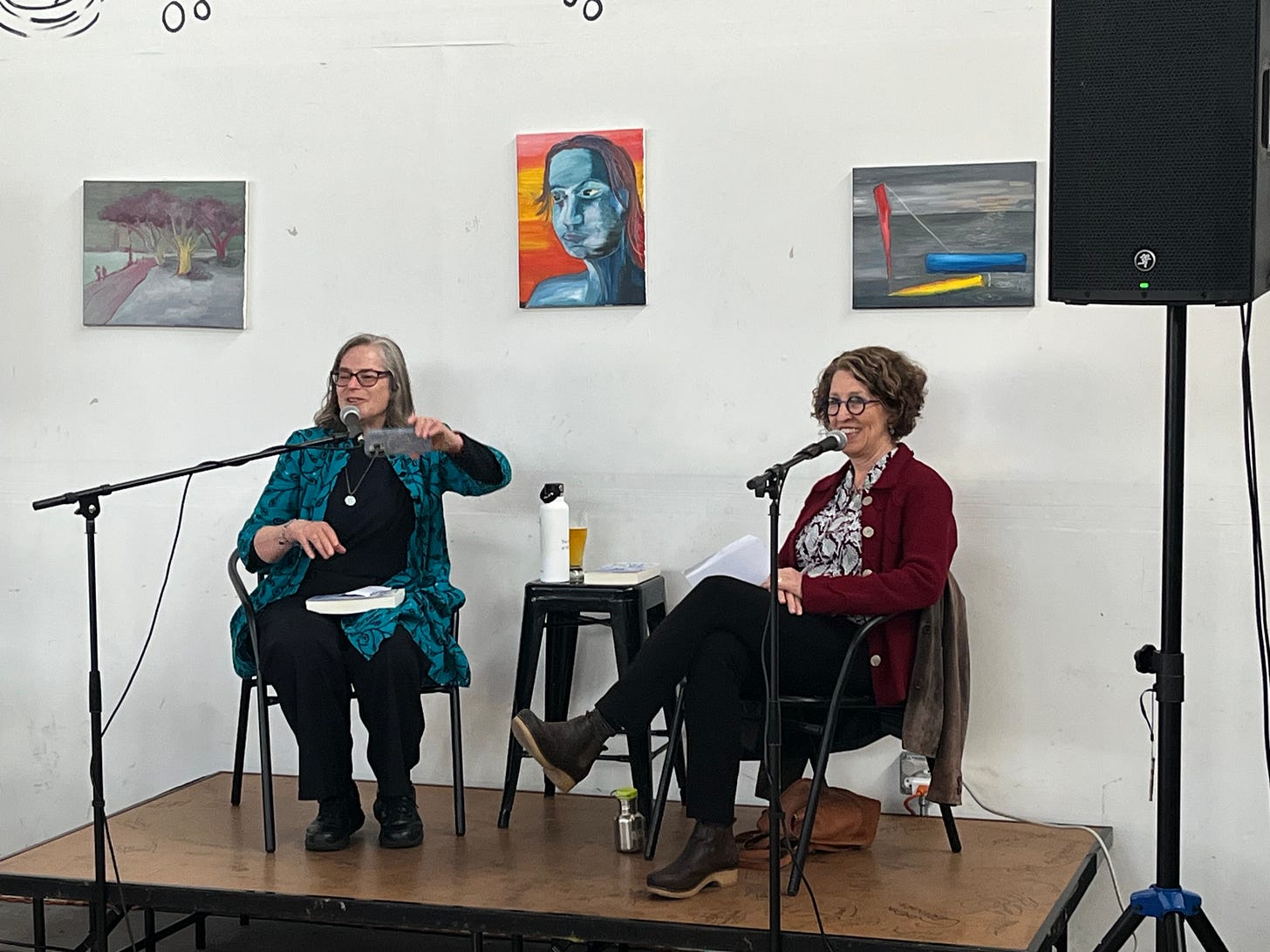 Two women seated on top of a low platform with mikes and books