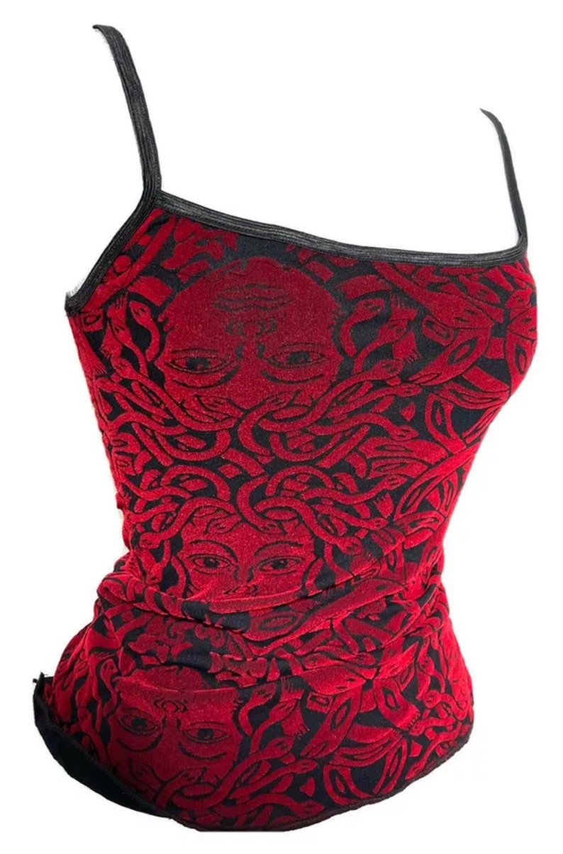 May include: A red and black camisole top featuring a Medusa face pattern. The top has thin black straps and trim. The fabric has a velvet-like texture. The design is a repeating pattern of Medusa's face with snakes. May include: A red and black camisole top featuring a Medusa face pattern. The top has thin black straps and trim. The fabric has a velvet-like texture. The design is a repeating pattern of Medusa's face with snakes.