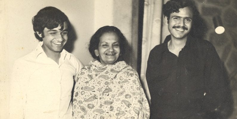 Three people smiling widely at the camera: from the left to the right: Agha Shahid Ali wearing a white shirt, Begum Akhtar wearing a paisley shawl, Saleem Kidwai wearing a dark shirt. The picture is black and white.