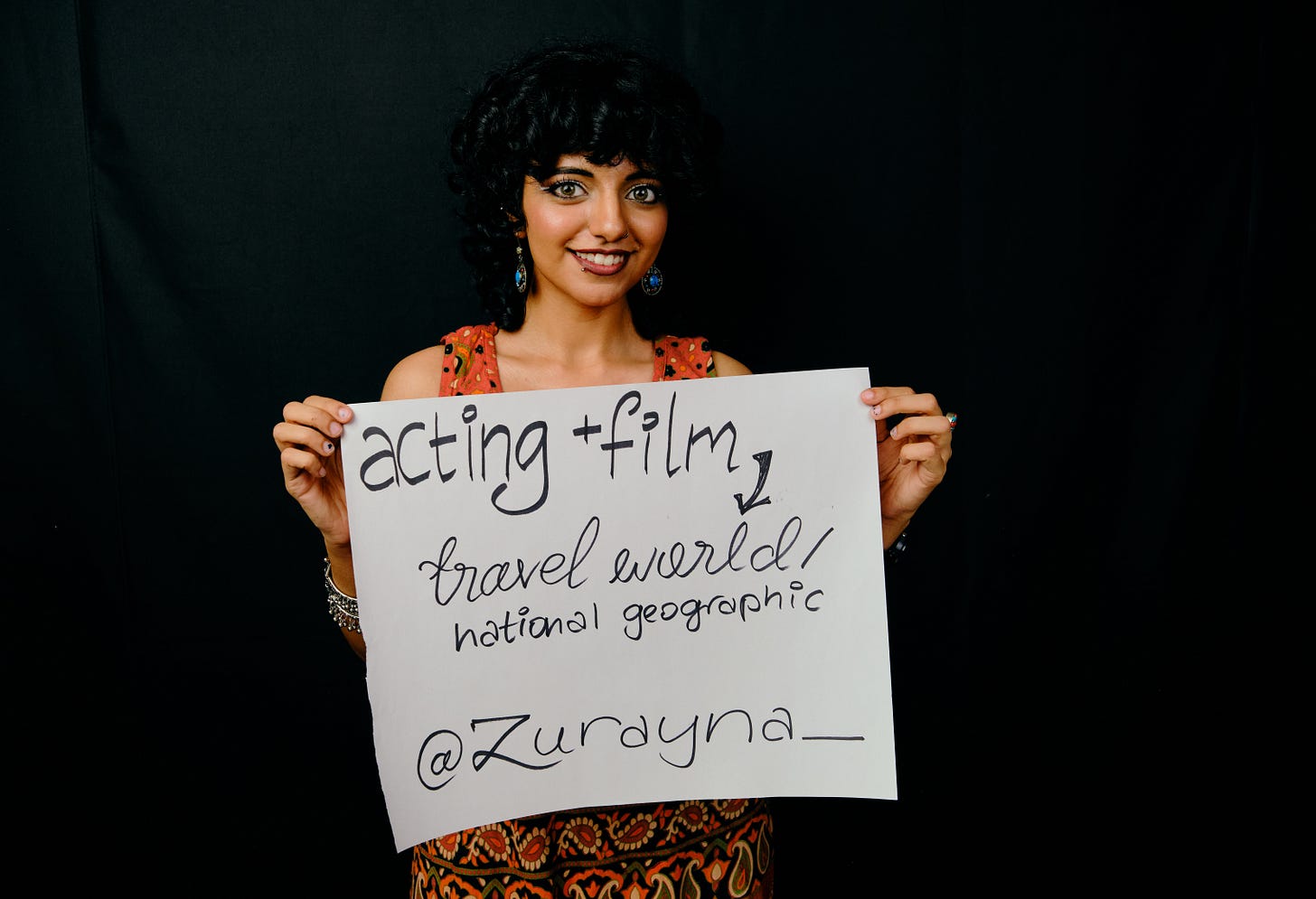 A dreamer at Dreams & Obstacles NYC 1 holds a handwritten sign about acting, filmmaking, and traveling the world.