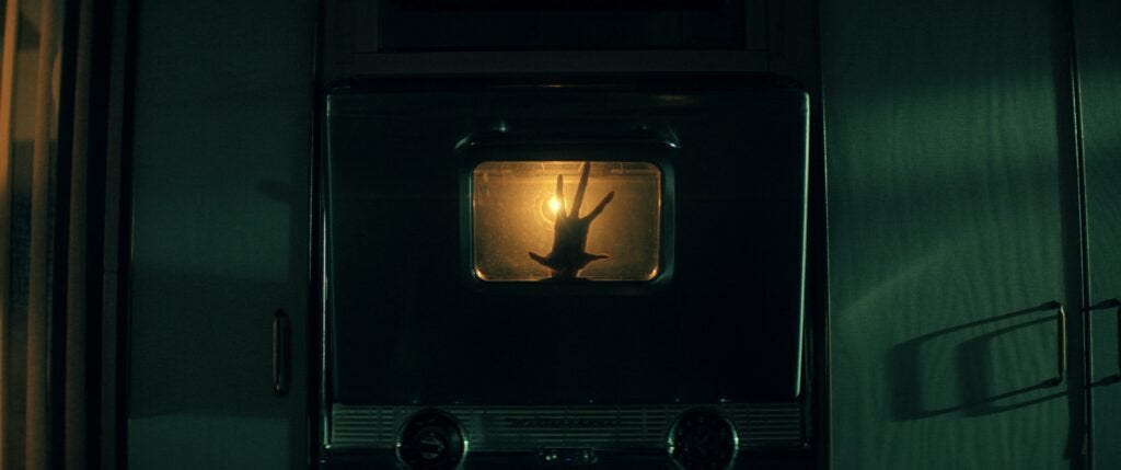 The hand of a strange creature pressing against the inside glass of a stove in The Boroughs on Netflix. 