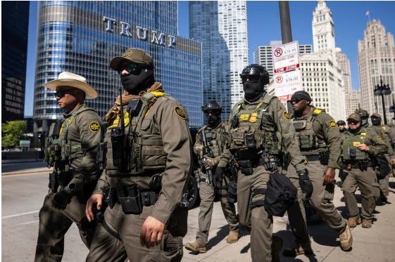 This image depicts a group of uniformed tactical officers marching in formation down a city street during the day. The setting is clearly identifiable as Chicago, with the Trump International Hotel & Tower visible in the background. The officers are heavily equipped with tactical vests and gear, and several have their faces obscured by masks. One officer on the left is wearing a cowboy hat.