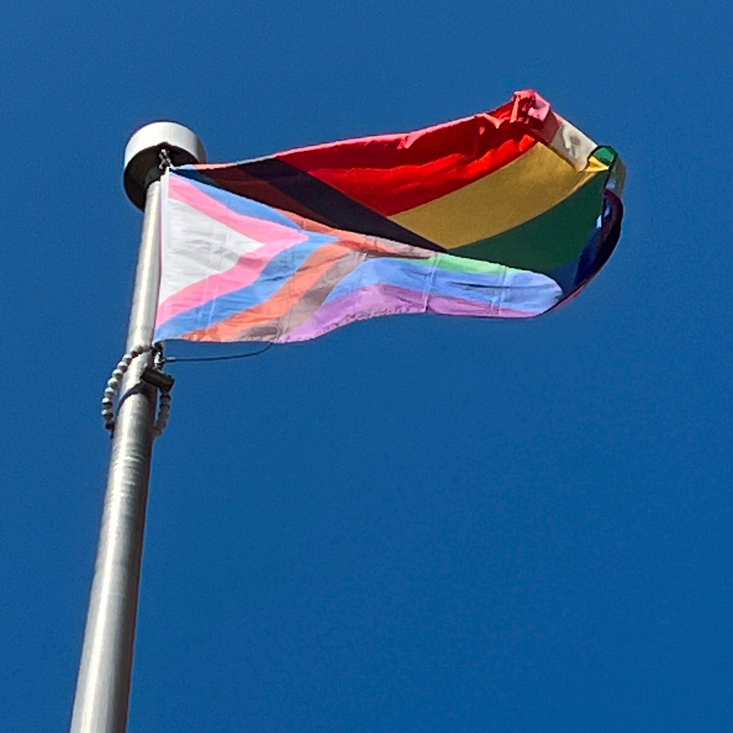 a pride flag flapping high in the sky against a blue sky a pride flag flapping high in the sky against a blue sky