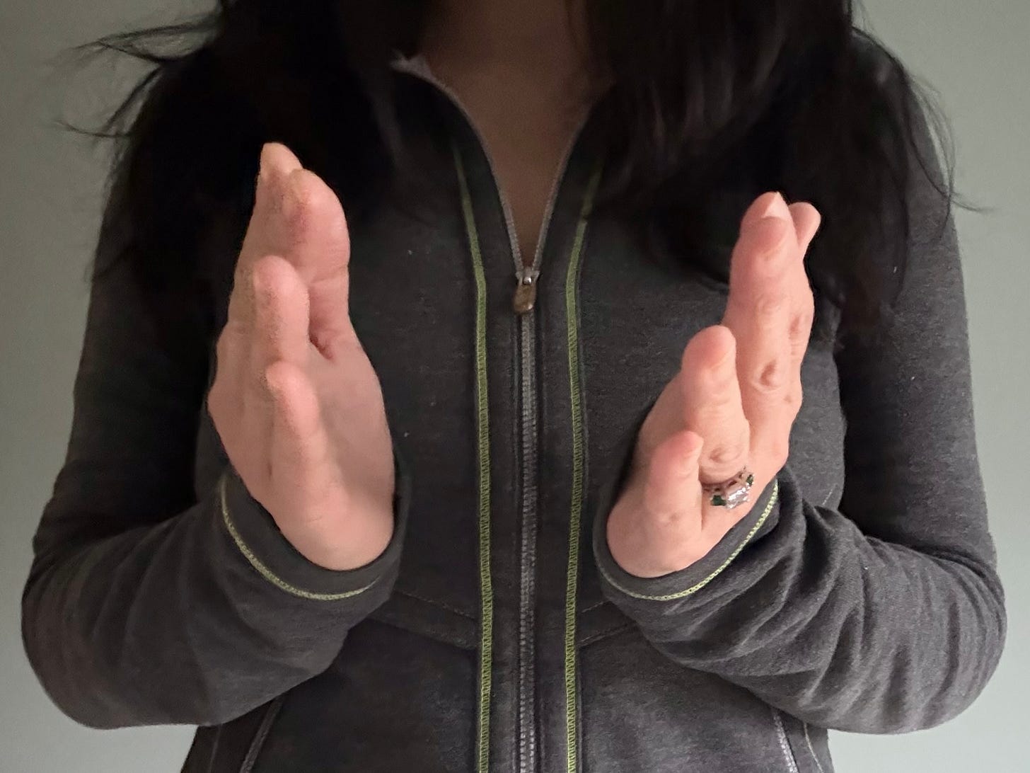 Close-up of a person in a dark zip-up jacket holding both hands upright in front of their chest, positioned as if about to clap.