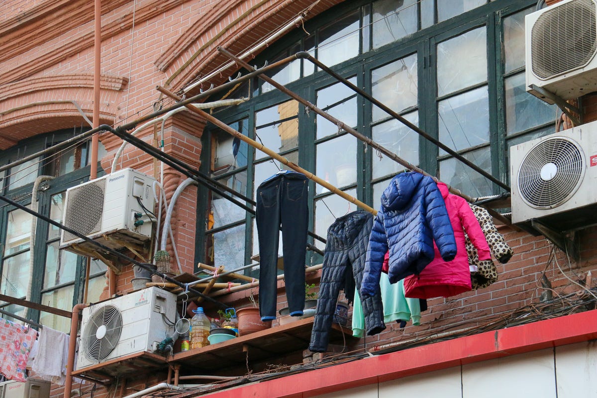 Heavy jackets and pants hang from bamboo poles outside apartment windows, flanked by air conditioning units. Practical life against the grit of dense city dwelling.
