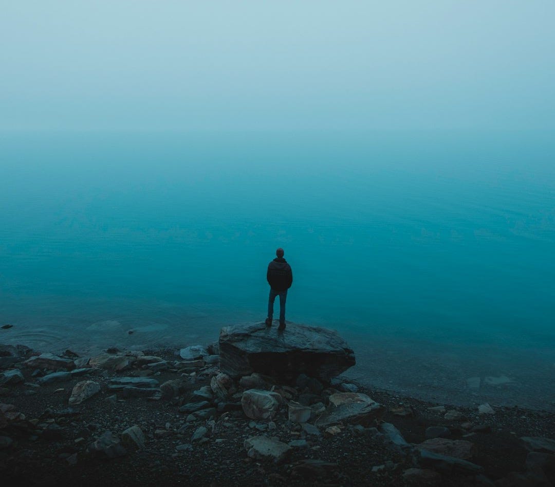 man standing on rock near body of water man standing on rock near body of water