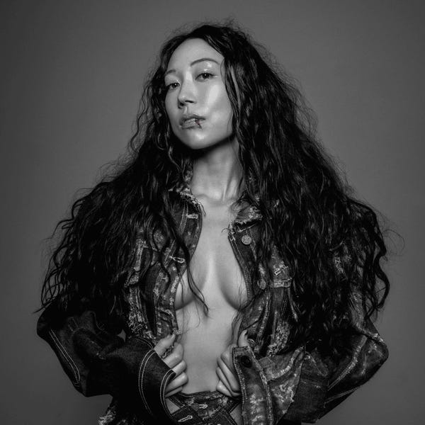 Album cover for Blood On the Silver Screen. A black and white portrait of SASAMI, whose long, wavy black hair cascades down over her shoulders. She wears a distressed denim jacket with a sliver of her chest and stomach exposed. There is a small streak of red blood on her bottom lip.