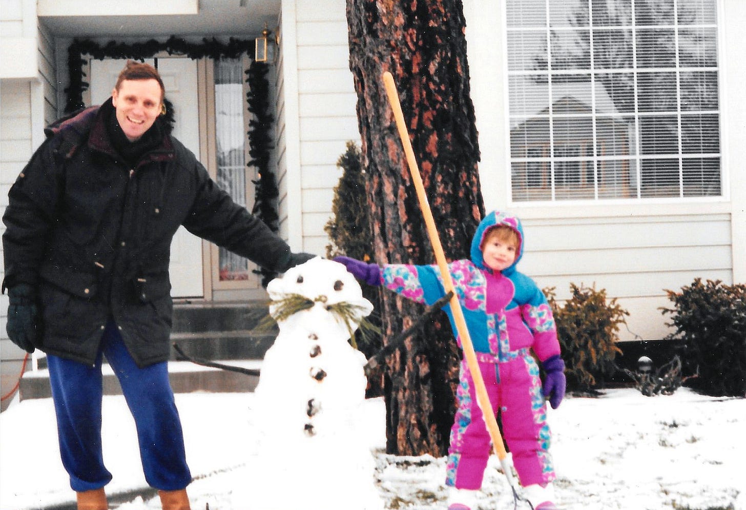The author's father and herself posing for a photo with a snowman in between them. The snowman has a big mustache made of pine needles.