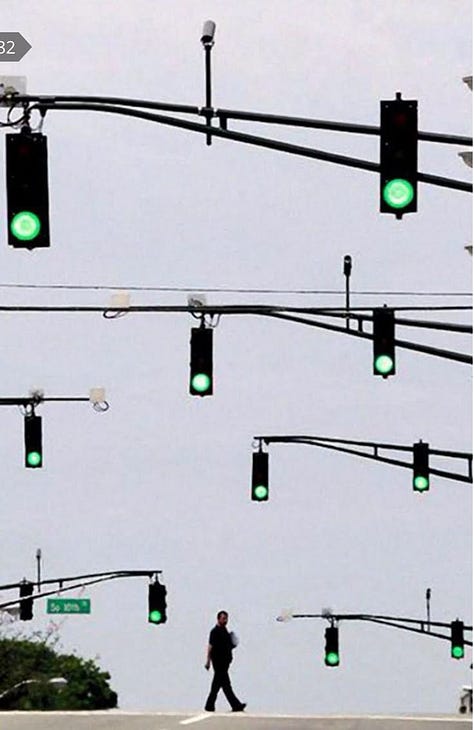 A series of symbols and signs including a the shadow of a green rafting tube, a lady bug on a four leaf clover, a street full of green stoplights, green birds on a line, a white arrow painted on the ground with green grass growing through it, a digital clock with the numbers 11:11