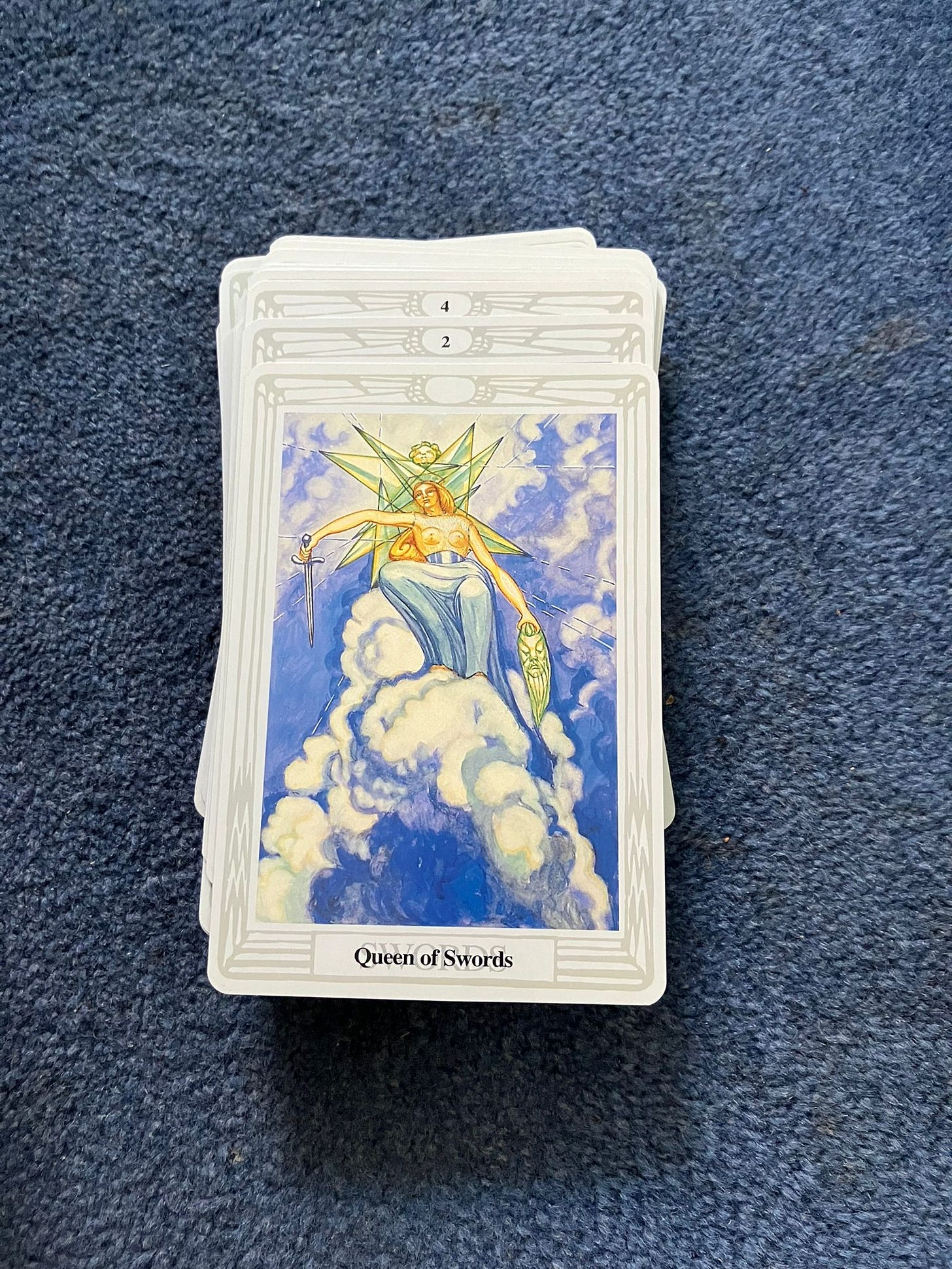 Queen of Swords tarot card from the Thoth Tarot by Aleister Crowley and Lady Frieda Harris, showing the crowned Queen of Swords seated in clouds with sword and mask, photographed for the Tarot DMs interview with bestselling author Joanne Harris.