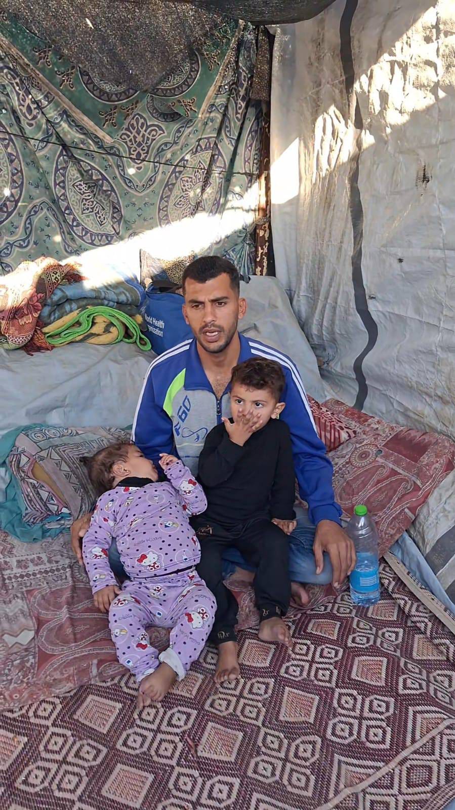 a man and two children in a refugee tent